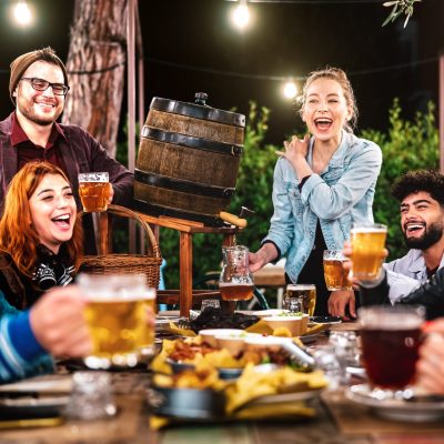 Happy men and women having fun drinking out at beer garden - Social gathering life style concept on young people enjoying hangout time together at night - Warm filter with shallow depth of field